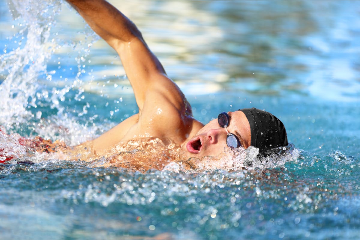 Man swimmer swimming crawl in blue ocean open water. Portrait of an athletic young male triathlete swimming crawl wearing cap and swimming goggles. Triathlete training for triathlon. Diemen zwemschool